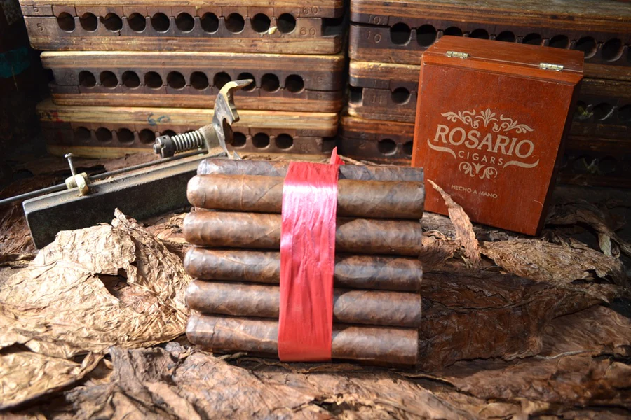 This is a image of a stack of 20 to 25 cigars. They are Rapped together with a thin colored paper ranging from cool whites to firey red wrappings they are forming a trianglur shape simular to a mountain or pyramid. While the Background shows the cigars placed on a feild of tabaco.